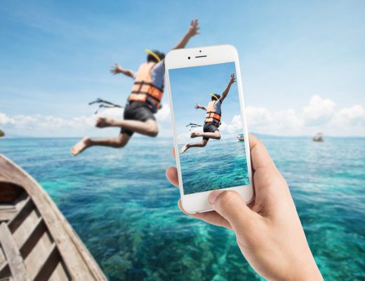 Man using photography app to take a picture of a man jumping out of a boat into the ocean